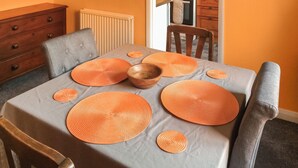 Une table à manger recouverte d’une nappe grise et agrémentée de sets de table orange, entourée de chaises en bois.