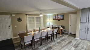 Een eethoek met een houten tafel en stoelen, een bank, een plafondventilator en een koelkast.