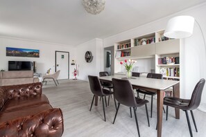 Un soggiorno moderno con un divano in pelle marrone, un tavolo da pranzo con sedie, una libreria e una televisione a schermo piatto.