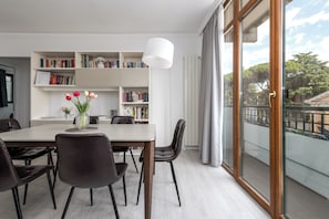 A modern dining area with a white table, dark chairs, a vase of flowers, and bookshelves filled with books.