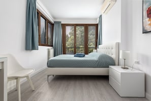 A bedroom with a bed, bedside table, chair, and a window with curtains.