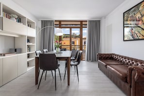 A modern living room with a dining area, a sofa, and a large window with curtains.