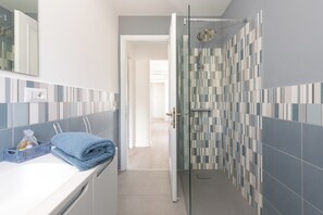 A bathroom with a shower, a towel, and a basket of toiletries.