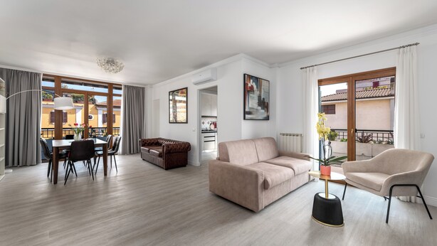 A modern living room with a sofa, armchair, dining table, and a balcony with a view. - La Casa del Tomo - Metro A - Private Parking - 6 Guests (Roma)