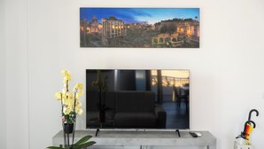 A flat-screen TV mounted on a wall above a modern sofa, with a potted plant and a decorative umbrella on the side. - La Casa del Tomo - Metro A - Private Parking - 6 Guests (Roma)
