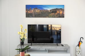 A flat-screen TV mounted on a wall above a modern sofa, with a potted plant and a decorative umbrella on the side.