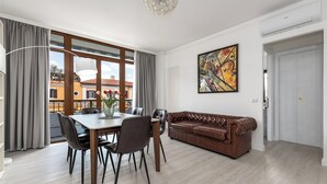 A modern living room with a dining table, leather sofa, and a large window. - La Casa del Tomo - Metro A - Private Parking - 6 Guests (Roma)