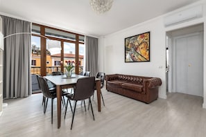 A modern living room with a dining table, leather sofa, and a large window.