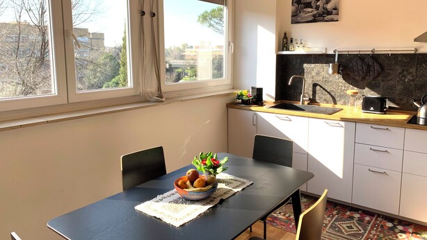 A modern kitchen with a dining table, chairs, a fruit bowl, and a view of the city through large windows. - Cozy apartment for two to four people near the Auditorium in Rome (Roma)