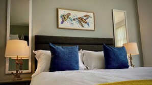 A hotel room with a large bed, two blue pillows, a framed artwork of sea turtles, and two bedside lamps. - The Horncliffe Hot Tub House (Blackpool)