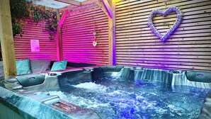 A hot tub with a heart-shaped light fixture on the wall, surrounded by wooden slats and a pink-lit backdrop. - The Horncliffe Hot Tub House (Blackpool)