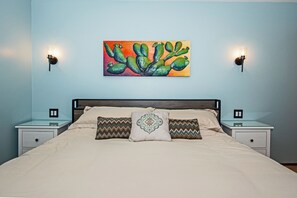 A bedroom with a bed, two nightstands, a wall-mounted painting, and two wall sconces.