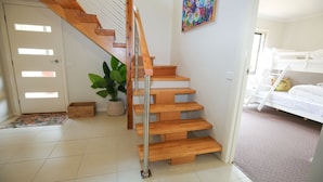 Eine Treppe mit Holzbalken und einem Metallgeländer, die zu einem Raum mit einem Etagenbett und einem farbenfrohen Bild an der Wand führt.