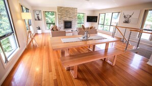 Ein geräumiges Wohnzimmer mit Holzboden, Kamin, Essbereich und großen Fenstern mit Blick ins Freie.