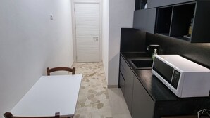 A compact kitchen with a white countertop, a microwave, and a sink. There is a door leading to another room and a small dining table with chairs. - Independent Penthouse in the Heart of Modena (Modena)