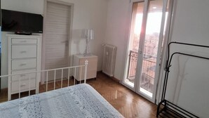 A bedroom with a bed, a dresser, a TV, a radiator, and a balcony with a view. - Independent Penthouse in the Heart of Modena (Modena)