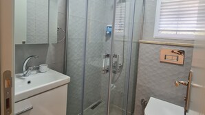 Une salle de bain moderne avec une douche à parois de verre, un lavabo blanc avec un porte-savon et des toilettes.