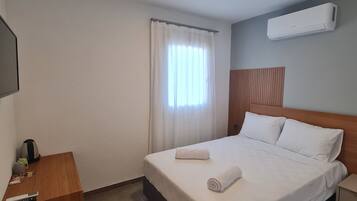 Una habitación de hotel con cama, escritorio, cesto de basura y unidad de aire acondicionado.