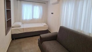 Une petite pièce, de taille modeste, comprenant un lit simple, un canapé et une fenêtre avec des rideaux.