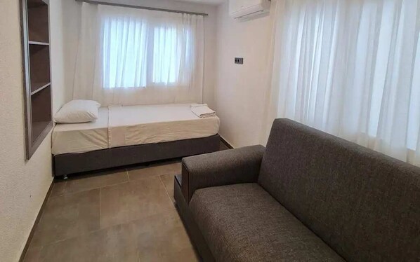 A small, compact room with a single bed, a sofa, and a window with curtains.