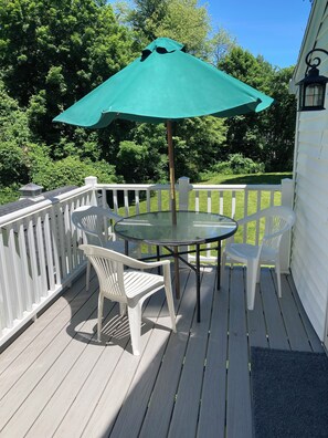 Une terrasse avec une table et des chaises en verre, un parasol vert et une rambarde blanche.