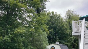 A small white building with a circular window and two large white tanks labeled 'Verson' on its side, surrounded by lush greenery and a grassy area.