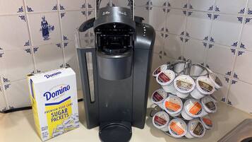 A coffee maker, a box of Domino sugar packets, and a collection of coffee pods on a kitchen counter.