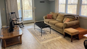 A living room with a sofa, a coffee table, a wooden side table, a chair, and a window with blinds.