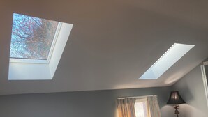 A bedroom with skylights, a window with curtains, and a floor lamp.