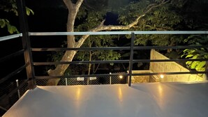 Un balcon avec une rambarde en métal, une vue sur les arbres et un lampadaire en arrière-plan.