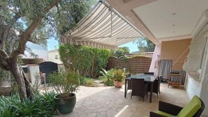 Un espace patio aménagé avec une table et des chaises, entouré de plantes en pot et agrémenté d’une pergola.