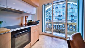 A modern kitchen with wooden cabinets, a stainless steel range hood, and a large window offering a view of a European-style building. - Port of Nice - Scooters Included (Nice)