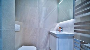 A modern bathroom with a toilet, a sink, and a hand sanitizer dispenser. - Port of Nice - Scooters Included (Nice)