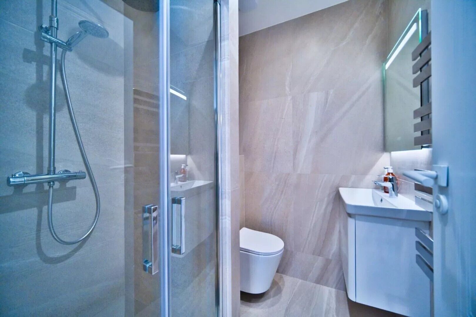 Une salle de bain moderne avec une douche à parois de verre, des toilettes blanches et un lavabo avec un miroir.