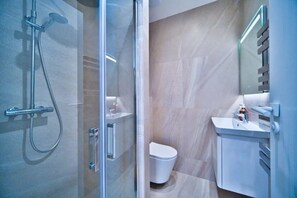 Un baño moderno con cabina de ducha de vidrio, inodoro blanco y lavamanos con espejo.