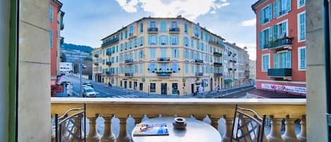 Un balcon avec une table et des chaises, donnant sur un immeuble à plusieurs étages doté de balcons et offrant une vue sur la rue.