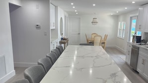 A modern kitchen with white cabinets, a marble island, and a dining area with grey chairs. - 3-bedroom mobile home in soothing Key Largo with WiFi, AC (Key Largo)