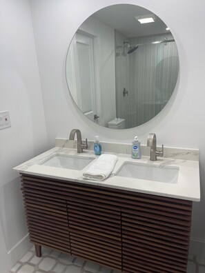 A bathroom with a double sink vanity, a round mirror, and a shower visible in the background. - 3-bedroom mobile home in soothing Key Largo with WiFi, AC (Key Largo)