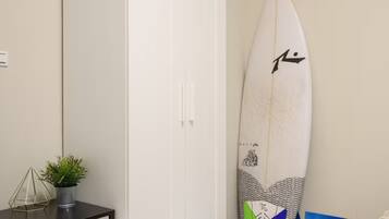 A bedroom with a white wardrobe, a small bedside table with a plant, and a surfboard leaning against the wall.