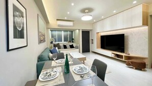 Una sala moderna con comedor, un televisor de pantalla plana grande y un sofá con cojines.