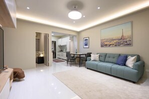 A modern living room with a green sofa, a dining table, and a kitchen in the background.