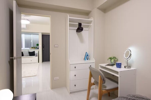 A bedroom with a white wardrobe, a desk with a mirror, and a chair.