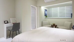 Una habitación de hotel moderna con una cama, un escritorio con una silla, una mesita con una planta y una ventana con persianas.
