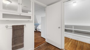 Een hotelkamer met een houten vloer, witte muren, een bed met witte lakens, een badkamer met een handdoekhouder en een open kledingkast.