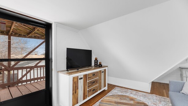 Een moderne loft slaapkamer met een groot raam, een houten tv-meubel, een ronde salontafel en een grijze bank.