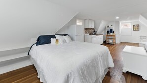 Een slaapkamer met een bed, witte wanden, een houten vloer, een bureau en een stoel.