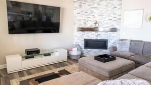 Un saló modern amb un televisor de pantalla plana penjat a la paret, un moble blanc d'entreteniment, un sofà gris i una catifes amb disseny.