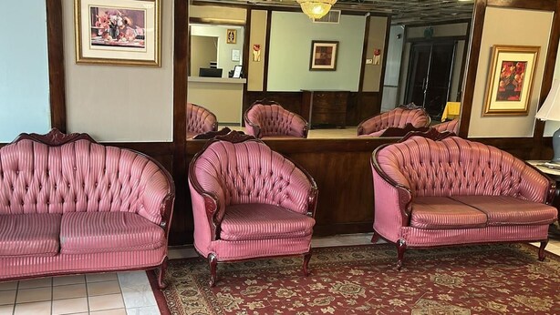 A room with three pink upholstered sofas and a wooden reception desk.