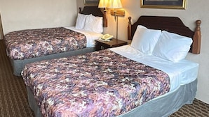 A hotel room with two beds, each with floral bedding, a nightstand with a lamp, and framed artwork on the walls.