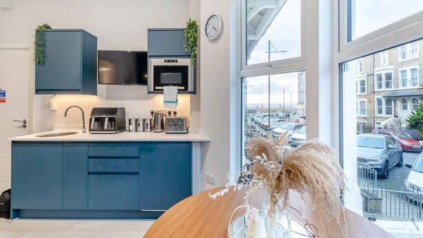 Cocina moderna equipada con microondas, tostadora y hervidor. Se aprecia una ventana con vista a automóviles estacionados y edificios.